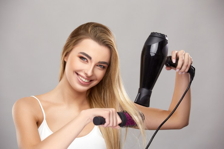 Donna che asciuga i capelli con il phon e una spazzola rotonda