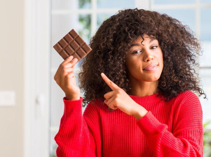 Ragazza riccia indica felice una barretta di cioccolato 