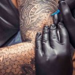 Tatuatore fa tatuaggio sul braccio di un uomo